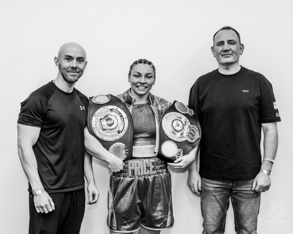 A black and white image of Pete Bell stands on the left of Lauren Price, who is grinning and has a huge boxing belt over each shoulder. Another man stands to the right.