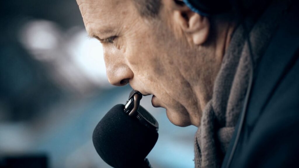 Side profile picture sees Peter Drury leaning into a mic, commentating on a football game.