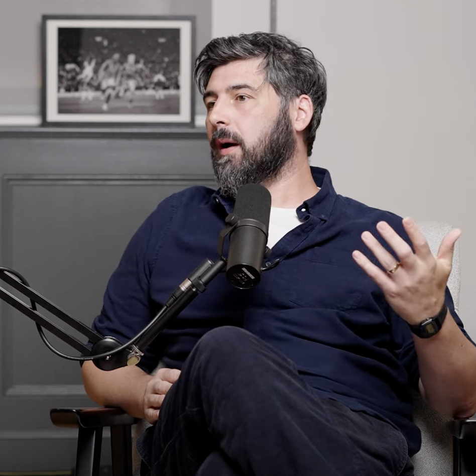 Alex Stewart sat in blue shirt, in a podcast studio.