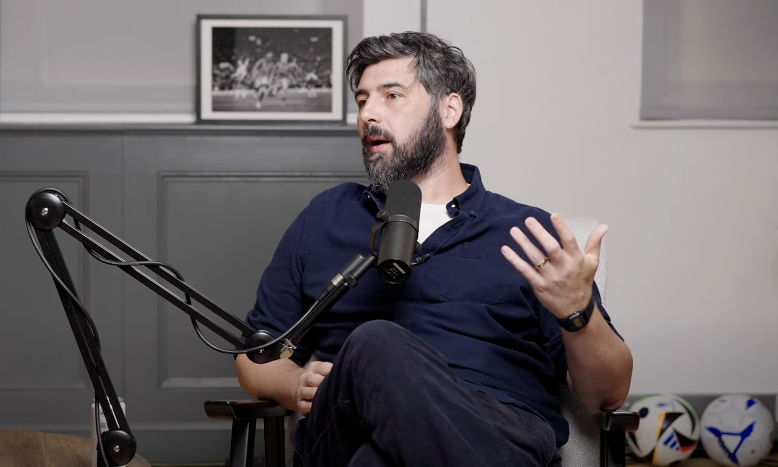 Alex Stewart sat in blue shirt, in a podcast studio.