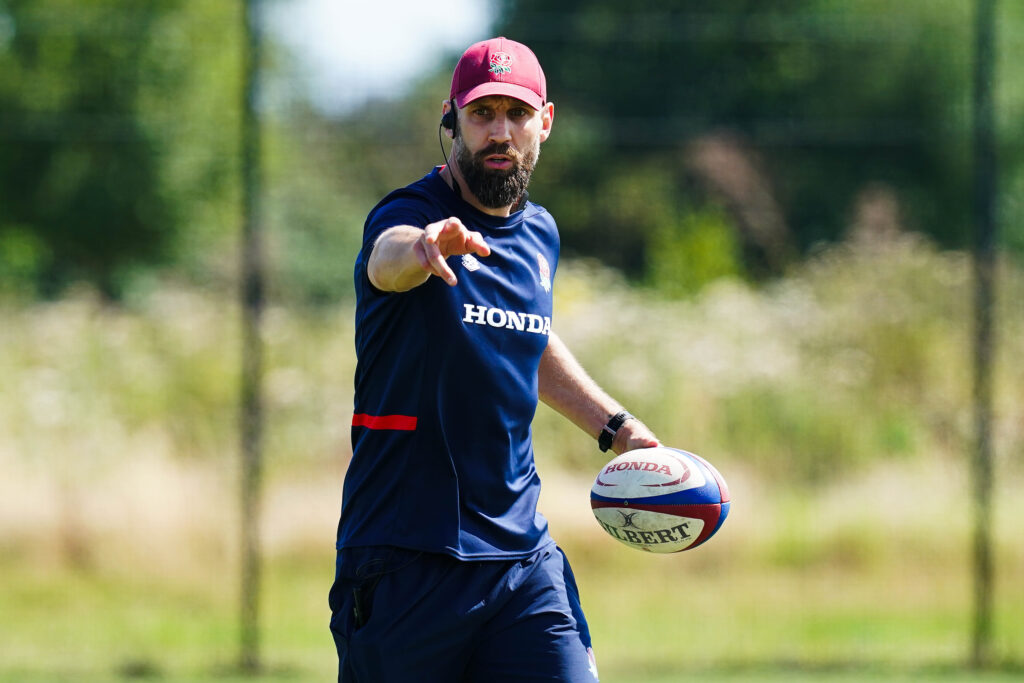 Jonathan Pendlebury coaching at an U18s England rugby training session with rugby ball in hand and pointing towards the camera.