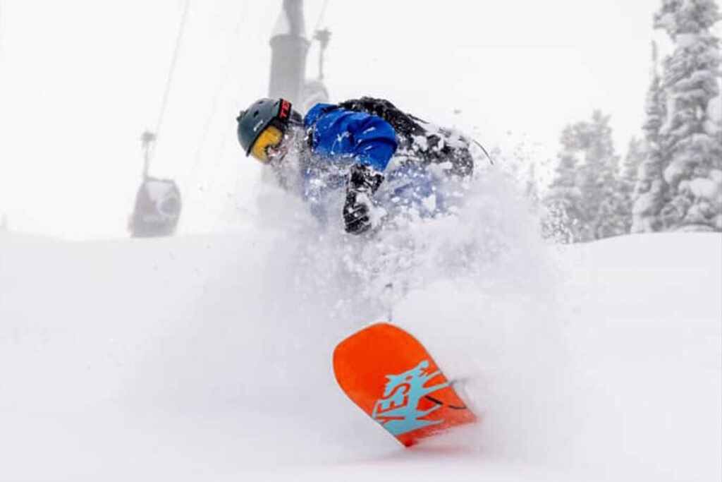 Luke Snow snowboarding on an orange snowboard.