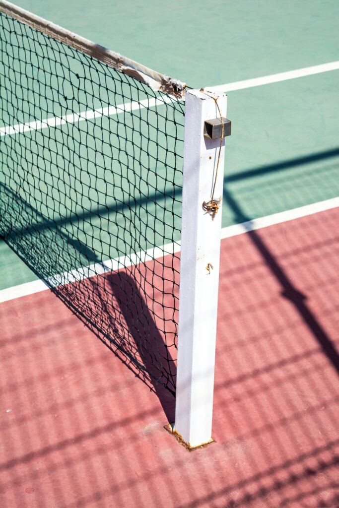 An image of a frayed black tennis net strung out across a red and green tennis court.