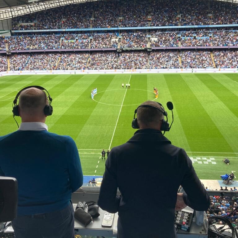 Photo from behind - that Shows Peter Drury (left) standing next to Jamie Carragher (right), getting ready to commentate on a Manchester City game at the Etihad during a minute of silence.