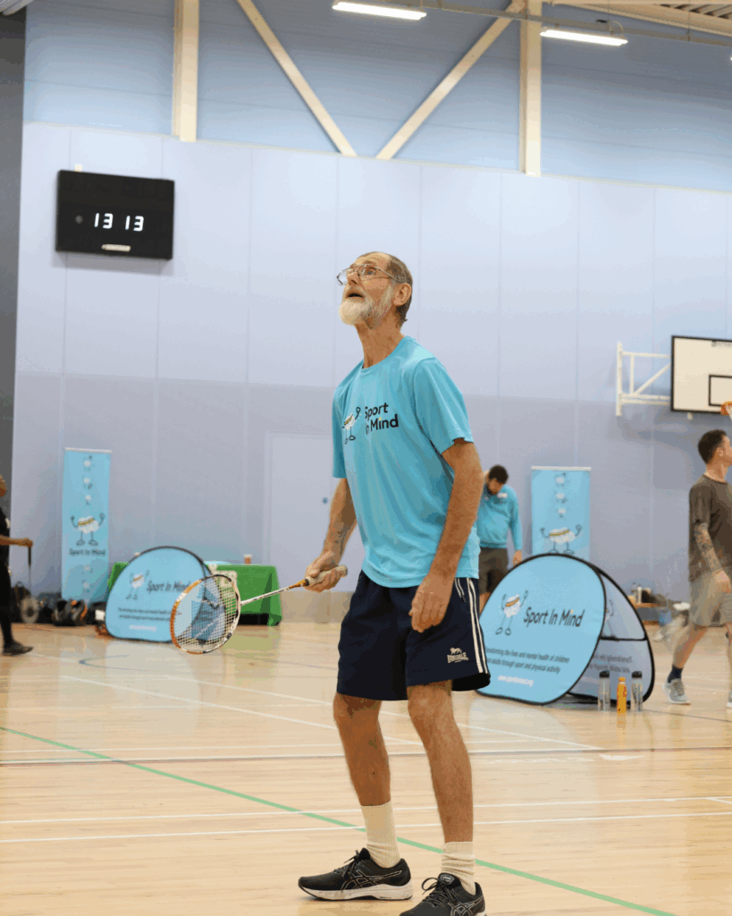 Man stares up whilst wearing a sport in mind tshirt, playing badminton in a sports hall