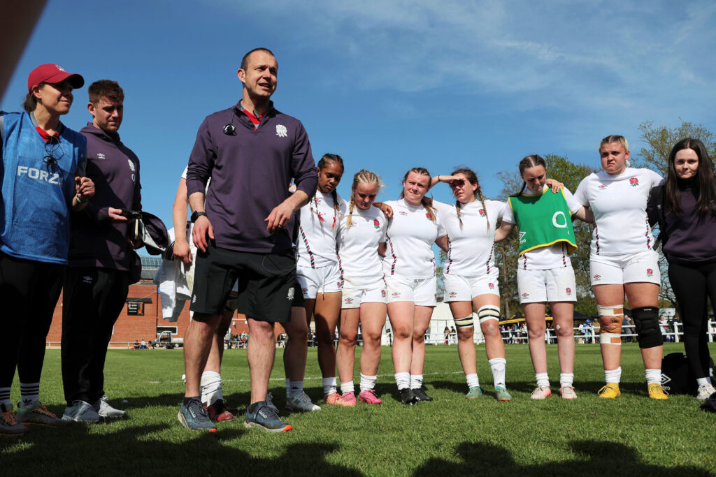 James Cooper in the middle of a team huddle of the England Women's U18s team at the 6 Nations festival