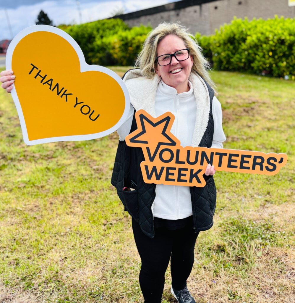 Volunteer - Karolyn Gaston - holding a 'Volunteers' Week'
week sign