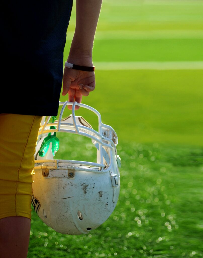 A gridiron football players arm is seen holding his helmet on a green field 

