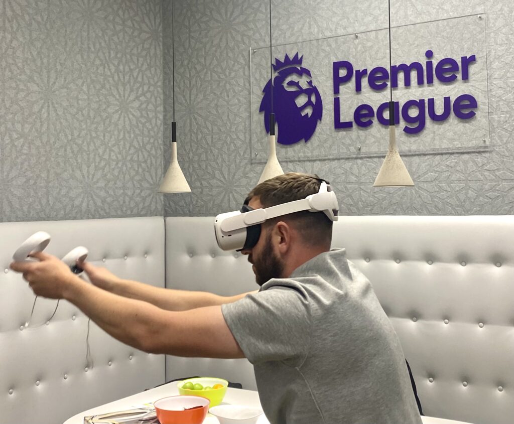 Picture shows a man using a VR headset in a room with a Premier League sign in the background