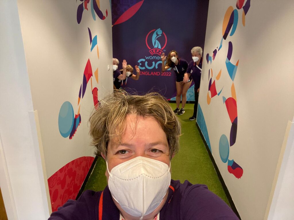 Julia Jone taking a picture in a corridor of Wembley Stadium with fellow volunteers in the background